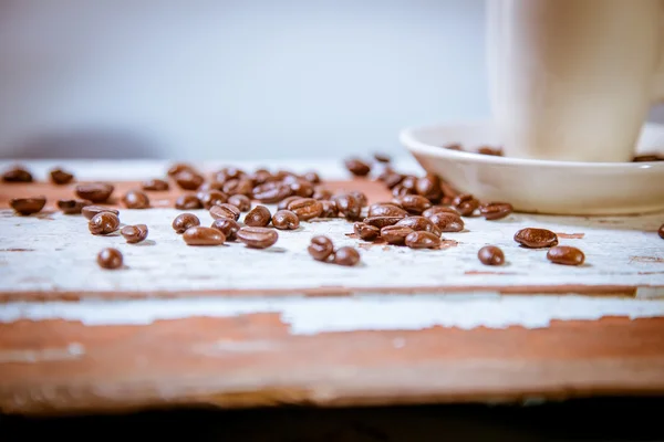 Chicchi sparsi di caffè in una tazza su uno sfondo di legno — Foto Stock