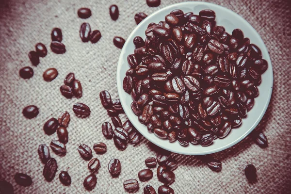 Grains éparpillés de café dans une tasse sur un fond en bois — Photo