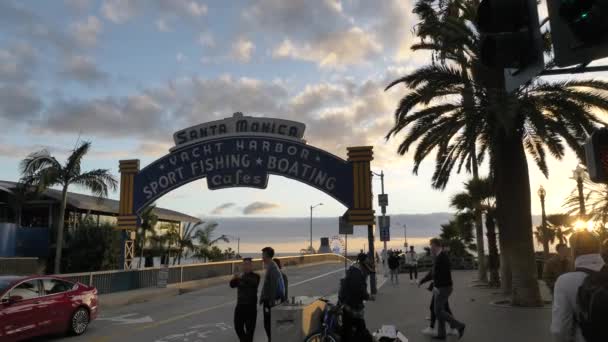 Muelle de Santa Mónica Entrada al crepúsculo o al atardecer en cámara de cámara lenta avanzando, los turistas caminando coches en movimiento. Santa Monica, California, EE.UU. - Enero 2020 — Vídeos de Stock