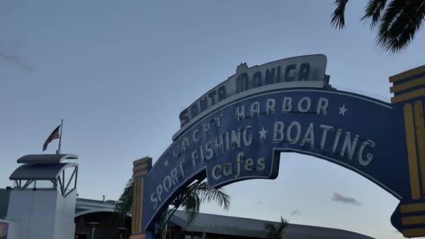 Santa Monica Pier Entré närbild vid skymning eller solnedgång tid i slow motion kamera rör sig framåt, turister gående bilar rör sig. Santa Monica, Kalifornien, USA - januari 2020 — Stockvideo