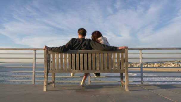 ヘルモサビーチピアのカップルの男性と女性有名なラ・ラ・ランドの風景、太陽のフレアの低い角度で海の美しい景色を楽しむ — ストック動画