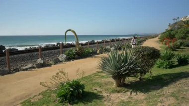 Yaşlı olgun bir kadın ağır çekimde yürüyor. Tren yolunun yakınındaki yolda mutlu. Güzel pasifik sahili, Orange County, San Clemente.