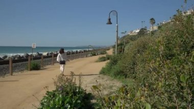 Yaşlı olgun bir kadın, tren yolunun yakınında mutlu bir şekilde yürüyor. Güzel pasifik sahili, Orange County, San Clemente.