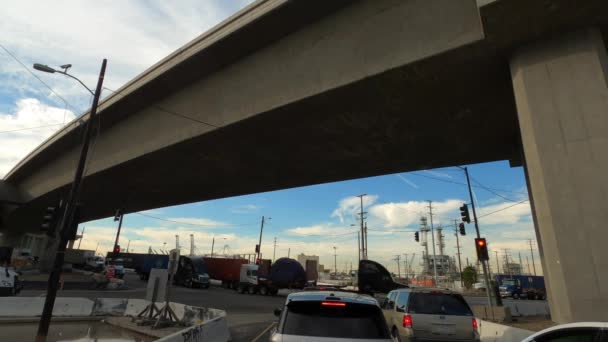 Long Beach California EUA - janeiro de 2020. Condução sob ponte passando caminhões perto da doca do porto com céu azul bonito e nuvens — Vídeo de Stock