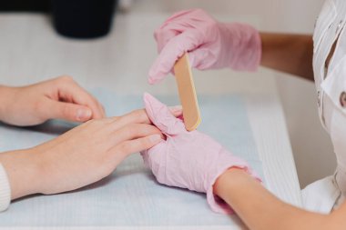 Manikür işlemi. Pembe lastik eldivenli bir usta tırnak törpüsüyle çivileri işliyor. Kadın elleri yakın..