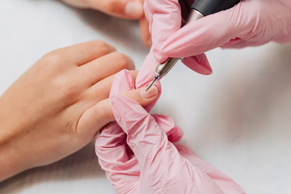 Manicure process. A master in pink rubber gloves polishes nails with an electric nail file. Female hands close up.