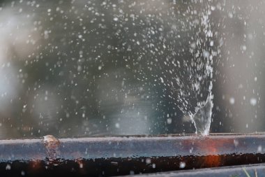 Metal bir su borusundaki delikten su fışkırıyor..