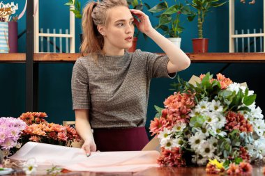 Çiçekçi bir buket kasımpatı yapar. Genç yetişkin bir kız dekorasyon için kağıt seçiyor..