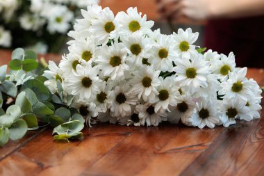 Tahta bir masanın üzerinde bir buket beyaz kasımpatı yatıyor..