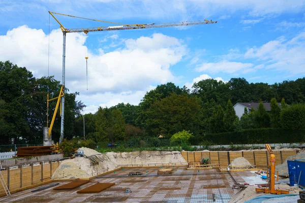 Construction crane on the construction of the foundation of a residential building. Blue sky with white clouds and green trees in the background.