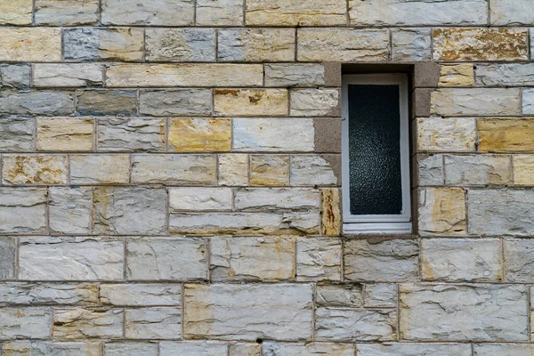 A fragment of a gray stone wall with window made of hewn stone of a rectangular shape. Close up.