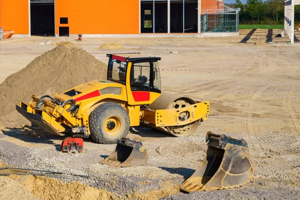 Yellow construction roller on a construction site. Excavator buckets on the ground. A bright sunny day.