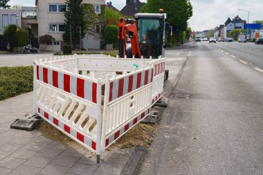 Şehir yolundaki tamirat sırasında kırmızı ve beyaz çitler. Arka planda küçük bir kazıcı var. Arabalar yol boyunca gider..