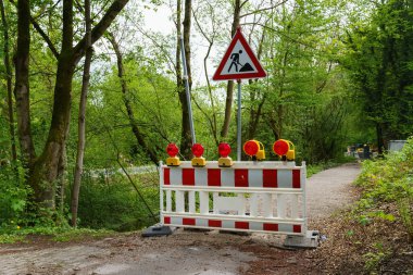 İnşaat alanının önündeki kırmızı ve beyaz taşınabilir bariyer. Kırmızı ışıklar ve yol çalışması tabelası.