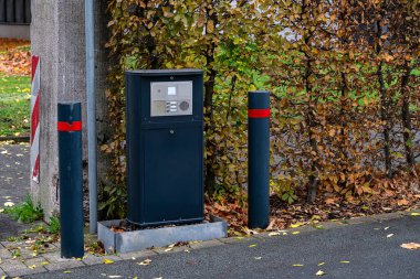Kapıdaki modern bir dahili telefon canlı bir sonbahar yaprakları zeminine karşı. Çevredeki mevsimsel değişiklikleri vurgulayan kırmızı işaretli iki kutup interkom çerçevesi.