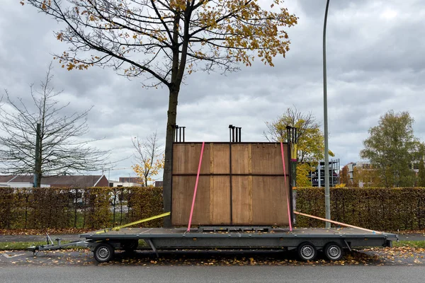 Dayanıklı ahşap bir yapı, renkli kayışlarla korunan bir karavana dikkatlice yüklenir. Gri bulutlar sessiz cadde üzerinde serin bir atmosfer oluştururken sonbahar yaprakları hışırdıyor..