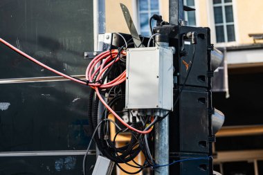 Bir trafik sinyal direğine karmaşık bir kablo ve kontrol kutusu monte edilir. Sahne, arka planda binalar ve açık gün ışığıyla kentsel bir alanda çekiliyor..