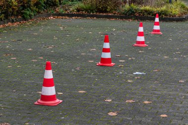 Dört parlak trafik konisi kaldırımlı bir otopark yüzeyinde düz bir çizgiye dizilmiştir. Külahları saran düşen yapraklar bölgede sonbaharın habercisidir. Ortalık sakin ve temiz..       