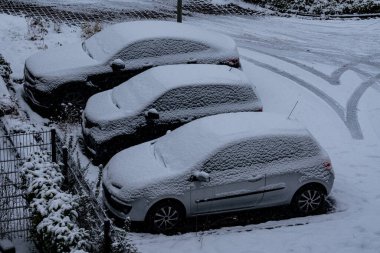 Otoparkta park edilmiş üç arabayı bir kar tabakası kaplıyor. Sahne, sabahın erken saatlerinde banliyö mahallesindeki kışın sessizliğini gösteriyor. Kar tüm araçları ve toprakları örtüyor..