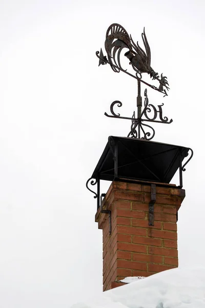 metal weather vane in the form of a rooster on the chimney pipe