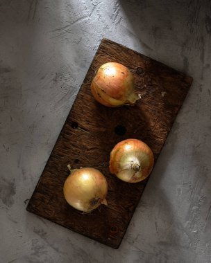 Köy tarzında beton bir arka planda eski ahşap bir tahtada soğanlar. Üst görünüm