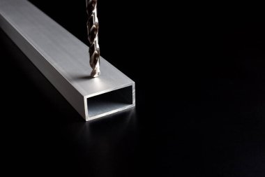 Karanlık yüzey arka planında alüminyum çelik profil tüpü delin. Metalde delikler açmak