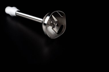 Karanlık yüzey arka planında izole edilmiş keskin bıçaklı elektrikli el blender başlığı.