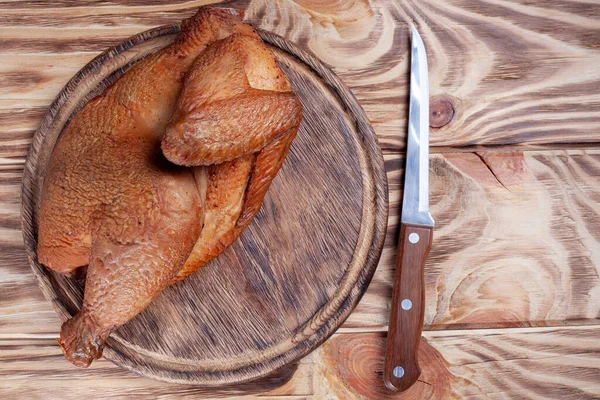 Keskin bıçakla ahşap kesme tahtasının üzerinde yarım tavuk tüttürdüm. Ahşap masada kızarmış tavuk. en üstteki görünüm