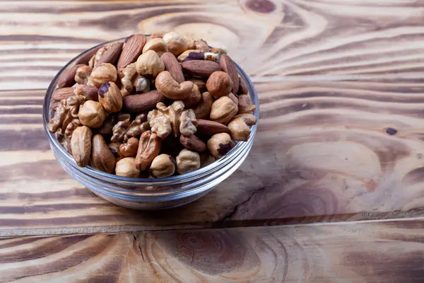 Assorted nuts in glass bowl. Mixed nuts for healthy diet on wooden table. Glass bowl on wooden background.