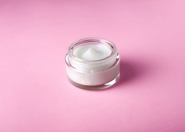 Cam kavanoz ve pembe arka planda vücut kremi olan beyaz şapka. Yüz kremi izole edilmiş şeffaf bir kavanoz. Cilt bakımı için kozmetik ürün.
