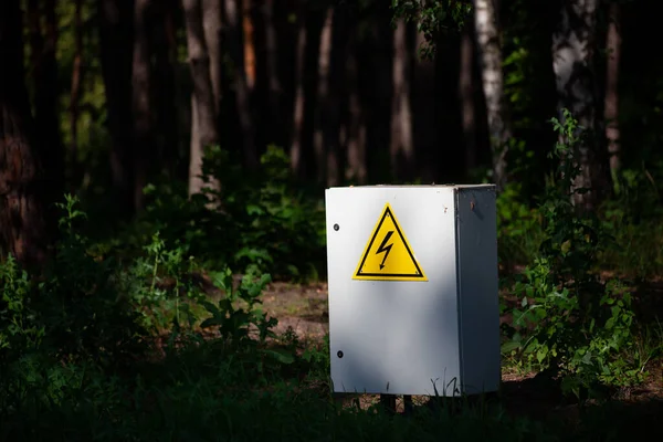 Close up Grey Hinged Power Supply Box in the forest. Outside electrical box with yellow danger warning sign. electricity in remote places.
