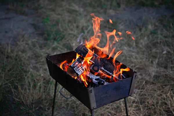 Een kleine opvouwbare draagbare vuurpijl gevuld met brandend hout. Koken op de grill. Veilig vuur in de natuur. Vlammen in vlammen. brandhout. — Stockfoto