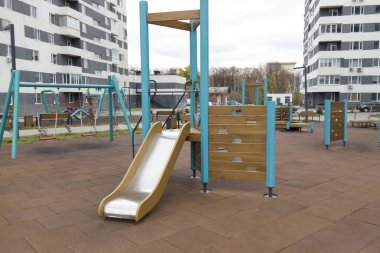 Çocuklar salıncakları, kaydırak ve tırmanma yapıları olan bir oyun parkında eğleniyorlar. Bölge bulutlu bir günde yüksek binalarla çevrilidir. Ukrayna. Kharkiv - 11 Kasım 2024