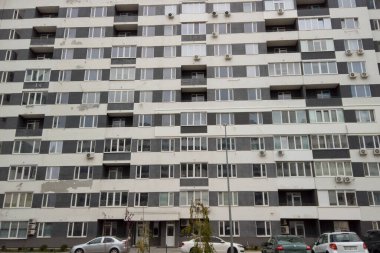 Çok katlı apartman çok sayıda penceresi ve ön cephesinde görünen havalandırma ünitesi ile yüksek duruyor. Arabalar binanın önünde park edilmiş. Ukrayna. Kharkiv - 11 Kasım 2024