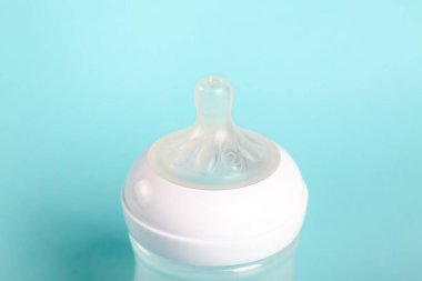 Bir bebek şişesi açık mavi arka planda oturur. Şişenin üstünde meme ucu var. Bu düzen bebekleri beslemek için hazır. Sahne yeni ebeveynler için önemli aracı gösterir.