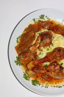 Tavuk bacağı, kasap soğanıyla pişirilmiş, patates püresi ile servis ediliyor. Yunan mutfağı, modern kaliteli baskı.