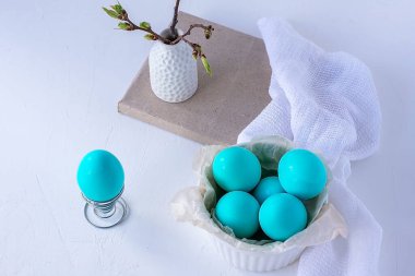 Paskalya yemeği konsepti. Beyaz bir tabakta boyanmış Paskalya mavisi yumurtalar ve beyaz arka planda vazoda bir filiz.
