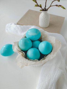 Paskalya yemeği konsepti. Beyaz bir tabakta boyanmış Paskalya mavisi yumurtalar ve beyaz arka planda vazoda bir filiz..