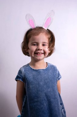 Mutlu Paskalyalar. Beyaz bir stüdyo geçmişinde üç yaşında, tavşan kulaklı bir kız. Neşeli çocuk.