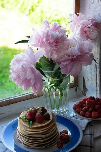 Pyszne domowe amerykańskie naleśniki ze świeżymi truskawkami na śniadanie. Talerz z naleśnikami i truskawkami, piwonie na tle starego wiejskiego drewnianego okna — Zdjęcie stockowe