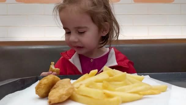 Το παιδί κάθεται σε ένα καφέ. Το κοριτσάκι με το κόκκινο μπουφάν τρώει ψήγματα και πατάτες. — Αρχείο Βίντεο