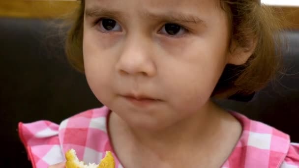 Çocuk bir kafede oturuyor. Kırmızı elbiseli ve beyzbol şapkalı küçük kız nugget ve patates kızartması yiyor. — Stok video