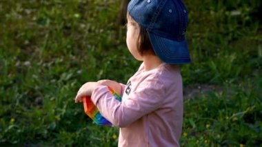 Sokakta bir çocuk pop it duyusal oyuncağıyla oynuyor. Kız renkli gökkuşağı yumuşak silikon kabarcıklarına basıyor. Stres ve endişe giderici. Moda oynatma oyunu