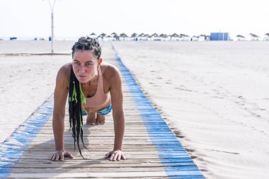 Olgun kadın eğitimi sahilde kalas ve karın egzersizi yapıyor. Boşluğu kopyala