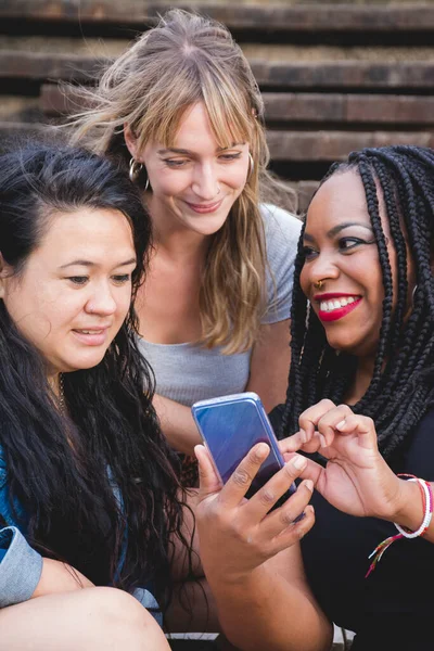 Group of smiling young women of diverse races sharing fun moments using smartphone. Concepts like diversity, friendship, companionship