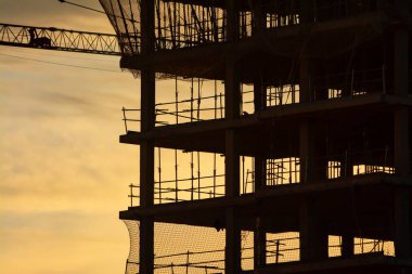 Gün batımında veya gün doğumunda sarı gökyüzü ve bulutları olan yapım halindeki bir binanın silüeti