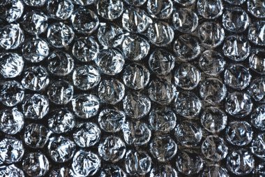 Tasarımların arka planı olarak desenli koyu bir kumaş üzerindeki kabarcıkların şeffaf plastik filmi