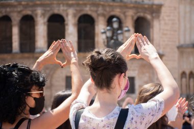 Valencia İspanya. 26 Haziran 2021 - İki kadın arka planda katedral ve kadın haklarını savunmak için elleriyle feminist bir sembol oluşturuyorlar.