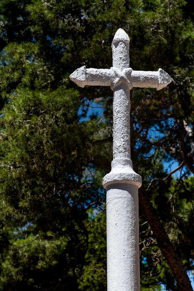 White painted stone christian cross with pine trees in the background. Vertical