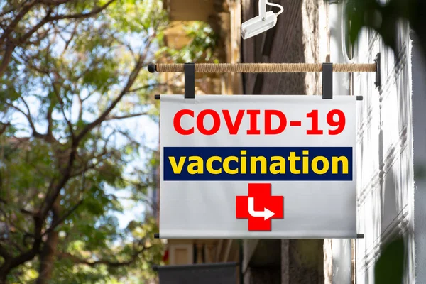 Hanging sign in the street with digital text informing of the covid 19 vaccination point, with an indicator arrow